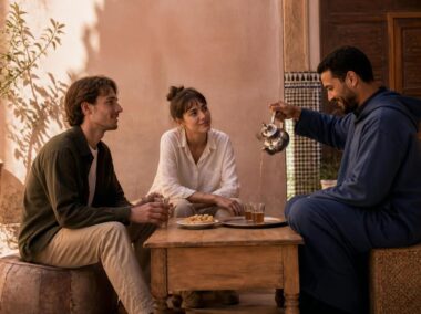 Moroccan host pouring mint tea for international visitors in a traditional courtyard
